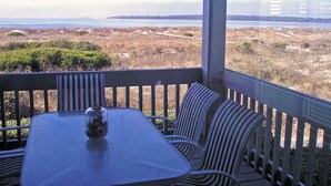 Un espace extérieur aménagé, abrité et doté d’une table et de chaises, offrant une vue sur un paysage côtier avec la mer et des collines lointaines à l’horizon.