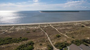 Vue aérienne d’une zone côtière avec une plage de sable, un ciel dégagé et une île au loin.