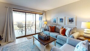 A living room with a sofa, coffee table, and a balcony with outdoor furniture. - Seabrook Exclusives | 1387 Pelican Watch (Johns Island)