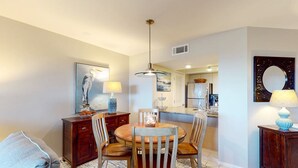 A dining area with a round wooden table, four chairs, a hanging light fixture, and a painting on the wall. - Seabrook Exclusives | 1387 Pelican Watch (Johns Island)