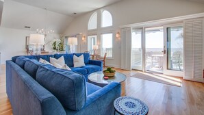A spacious living room with a blue sofa, a glass coffee table, and a view of a balcony with white shutters.