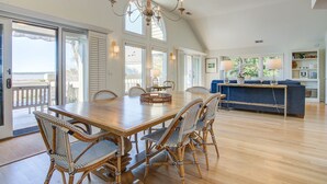 A spacious dining area with a wooden table and wicker chairs, a chandelier, and a view to the outside.