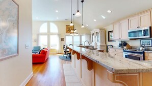 Una cocina moderna con una isla grande, iluminación colgante y vistas al área de estar.