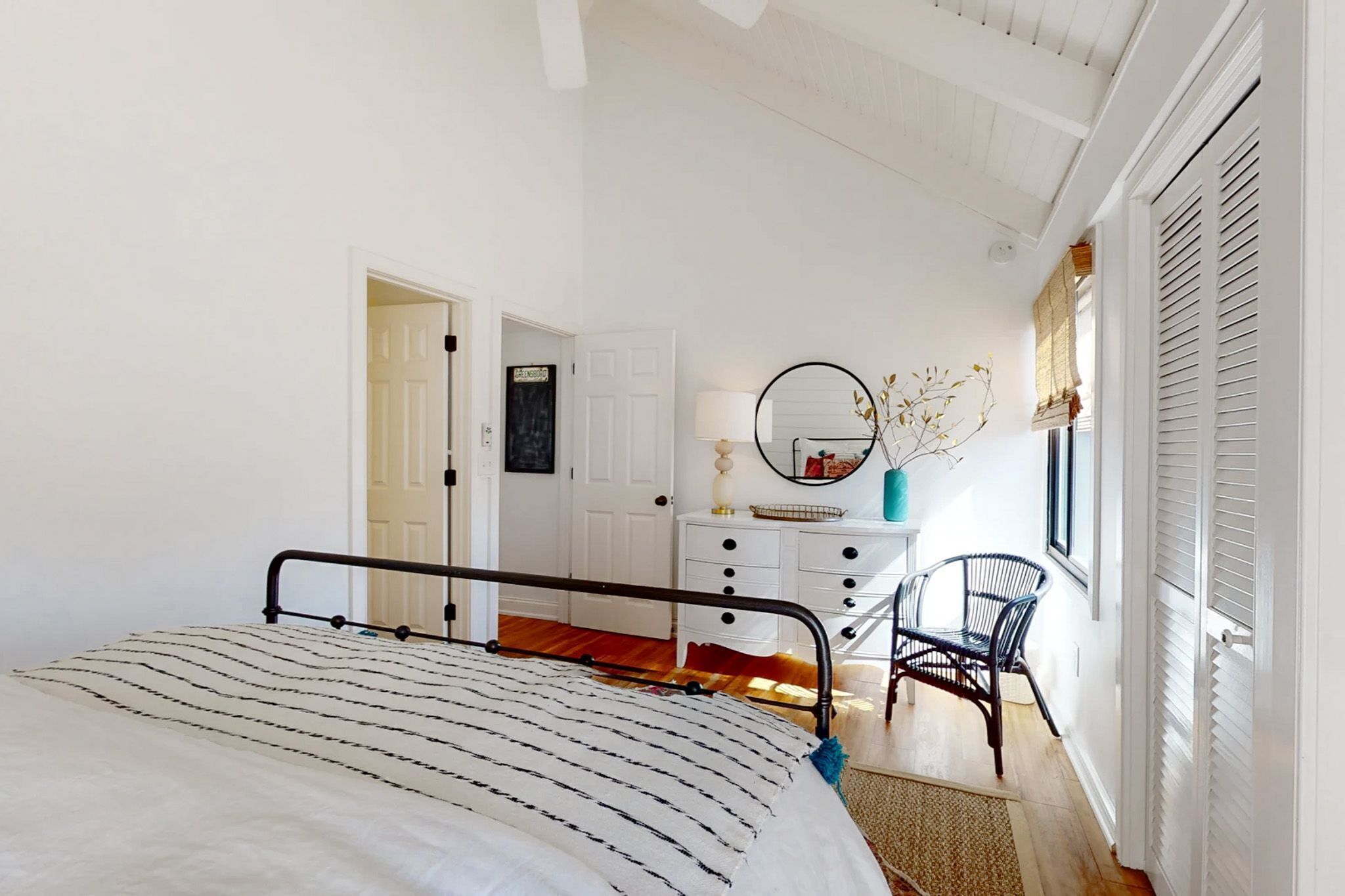 A bedroom with a bed, a dresser, a chair, and a window with shutters.