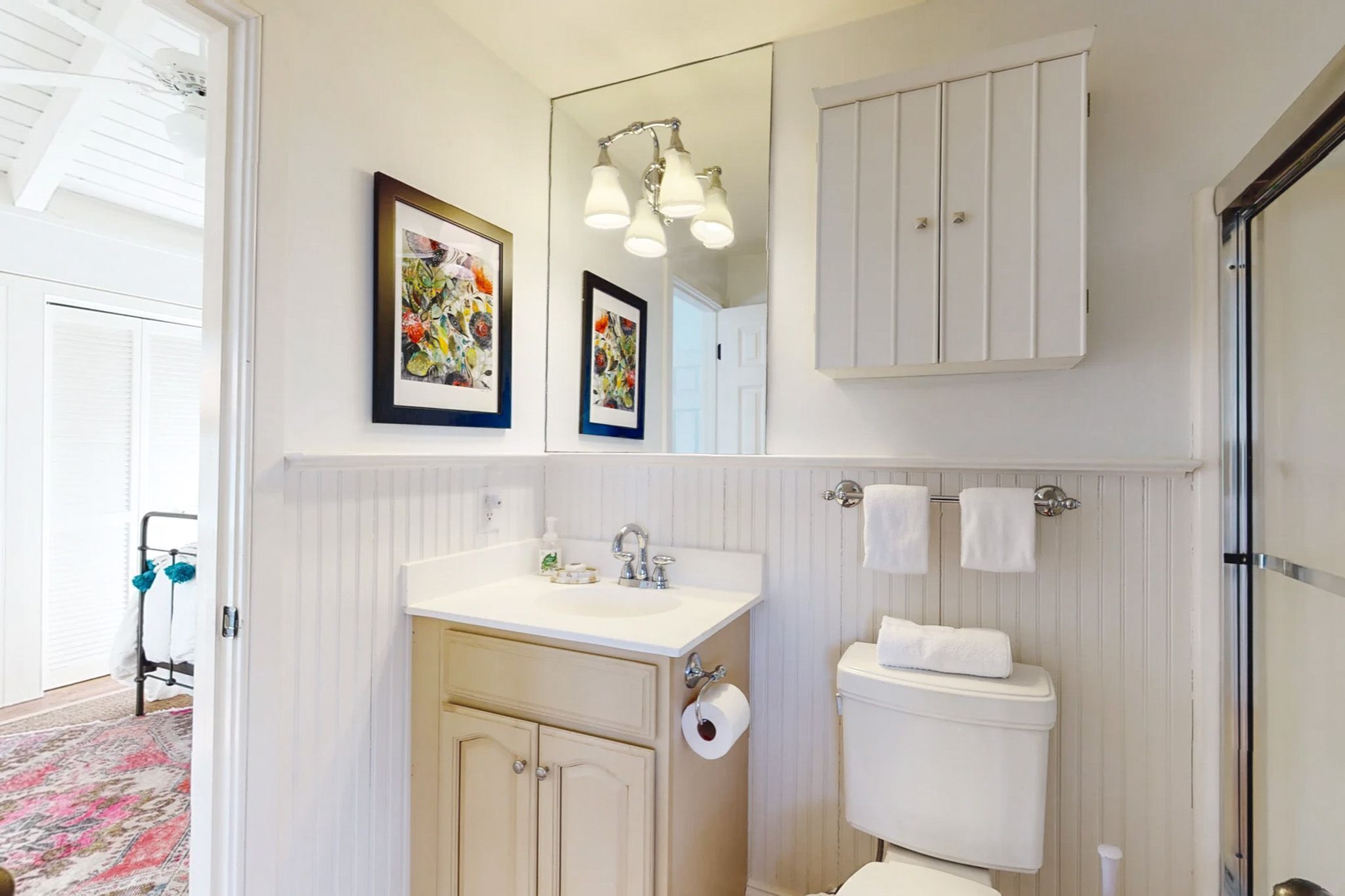 A bathroom with a white vanity, a toilet, a mirror, and two framed artworks.