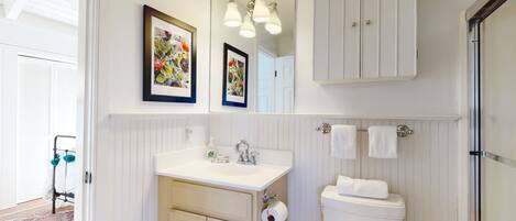 A bathroom with a white vanity, a toilet, a mirror, and two framed artworks.