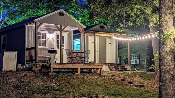 Eine kleine, eingeschossige Holzhütte mit einer Veranda und einer überdachten Sitzgelegenheit im Freien.