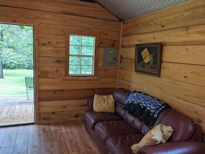 A wooden cabin interior with a leather couch, a window, and a framed picture on the wall. - Cypress Cabin "Tiny house" (Mammoth Spring)