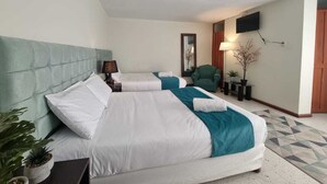 Ein Hotelzimmer mit zwei Betten, einem grünen gepolsterten Kopfteil, einem wandmontierten Flachbildfernseher und einem kleinen Tisch mit einer Lampe.