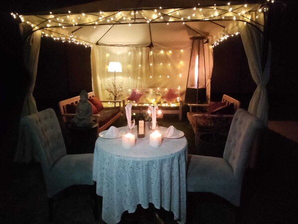 An outdoor dining area with a table set for two, surrounded by chairs, under a canopy with string lights. - Adriana Monet Collection (Arequipa)