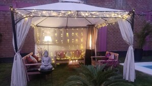 Ein überdachter Außenbereich mit Lichterketten, einer Buddha-Statue und einem kleinen Tisch mit Kerzen.