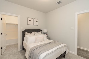 A bedroom with a bed, bedside table, lamp, and two framed pictures on the wall.