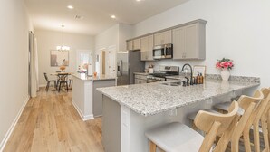 A modern kitchen with granite countertops, stainless steel appliances, and wooden bar stools. - Cozy NEW Home in the Heart of Lafayette! (Lafayette)