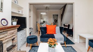 A living room with a TV, a fireplace, a dining area with chairs, and a staircase.
