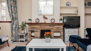 A living room with a fireplace, a television, and a white coffee table with a vase of flowers.