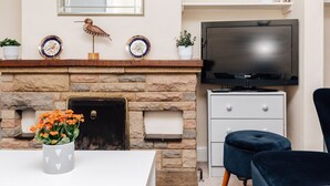 A living room with a stone fireplace, a flat-screen TV mounted above it, and a white cabinet to the right.
