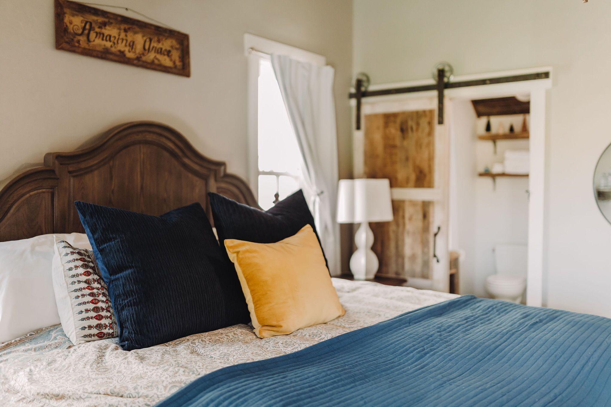 A bedroom with a wooden headboard, a bed with patterned pillows, a blue blanket, and a wooden door with a white curtain.