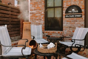 A cozy outdoor seating area with wicker chairs and a fire pit, set against a brick wall with a sign reading "The Lodge 37A Park Street".