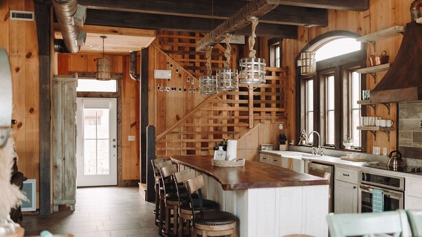 Een landelijke keuken met houten wanden, een bar met krukken, en een groot eiland.