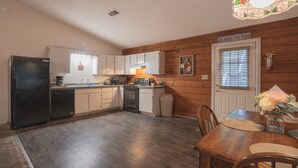 A compact kitchen with a refrigerator, stove, microwave, and sink. There's a dining table with chairs and a small vase of flowers. - Cabin I at Safe Harbor Brady Mountain on Lake Ouachita! (Royal)