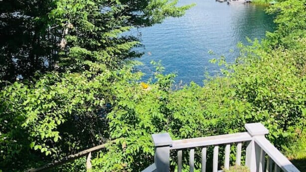 A view of a lake surrounded by dense greenery, with a wooden deck and a small table in the foreground. - Ever After <br>Lakefront Splendor (Florence)