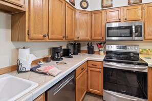 A kitchen with wooden cabinets, a stainless steel microwave, a stove, and various kitchen appliances.
