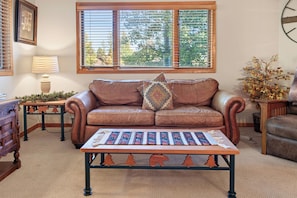 A living room with a brown leather sofa, a patterned rug, a wooden coffee table, and a window with blinds. - Spacious Breck Hideaway. Hot Tub. On Town Bus. (Breckenridge)