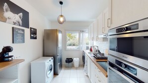 Eine moderne Küche mit eingebauter Waschmaschine, einem großen Kühlschrank, einer Spülmaschine und einer Mikrowelle. Ein Fenster lässt Tageslicht herein und bietet einen Ausblick nach draußen.