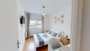 Ein Schlafzimmer mit Bett, Nachttisch, Lampe, Stuhl und einem Fenster mit Vorhängen.