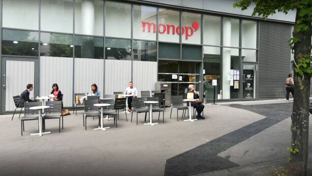 Ein Außenbereich mit Sitzgelegenheiten vor einem Gebäude, das ein 'monop' Schild zeigt.