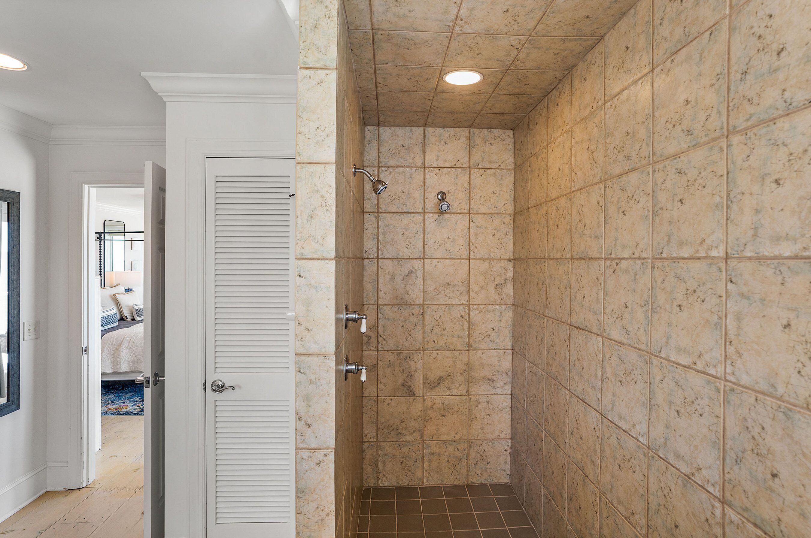 A walk-in shower with beige tiles, a white door, and a tiled floor.