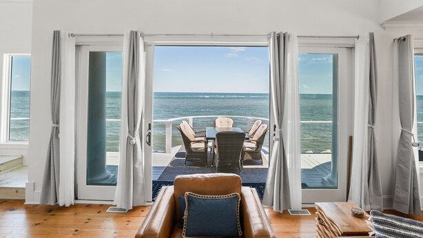 Ein Zimmer mit Meerblick, eine Essecke mit Stühlen und Tisch sowie ein großes Fenster mit Vorhängen.