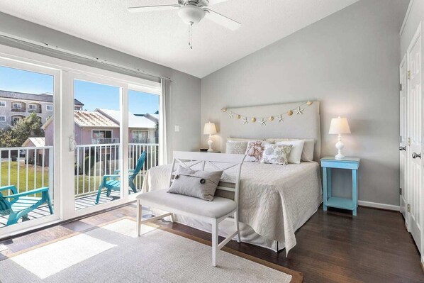 A bedroom with a large sliding glass door leading to a balcony, a bed with a headboard, two bedside tables with lamps, and a chair.