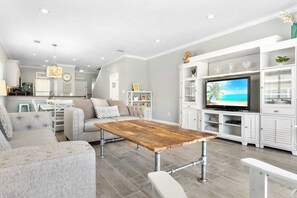 Un salon moderne avec un canapé gris, une table basse en bois et un téléviseur posé sur un meuble de télévision blanc.