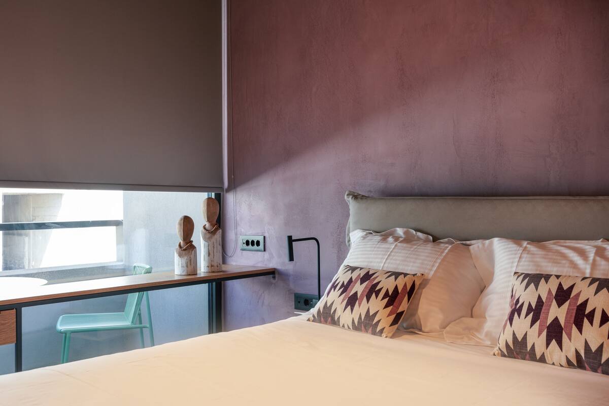 Un dormitorio con una cama, un escritorio y una silla. Se ve una ventana con vistas al exterior.