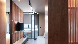 A modern hotel room with a wooden partition, a flat-screen TV, a sofa, and a desk with a chair. - Souda Plaza Collection (Chania)