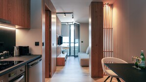 A modern kitchen with wooden cabinets, a built-in oven, and a dining area with a table and chairs. - Souda Plaza Collection (Chania)