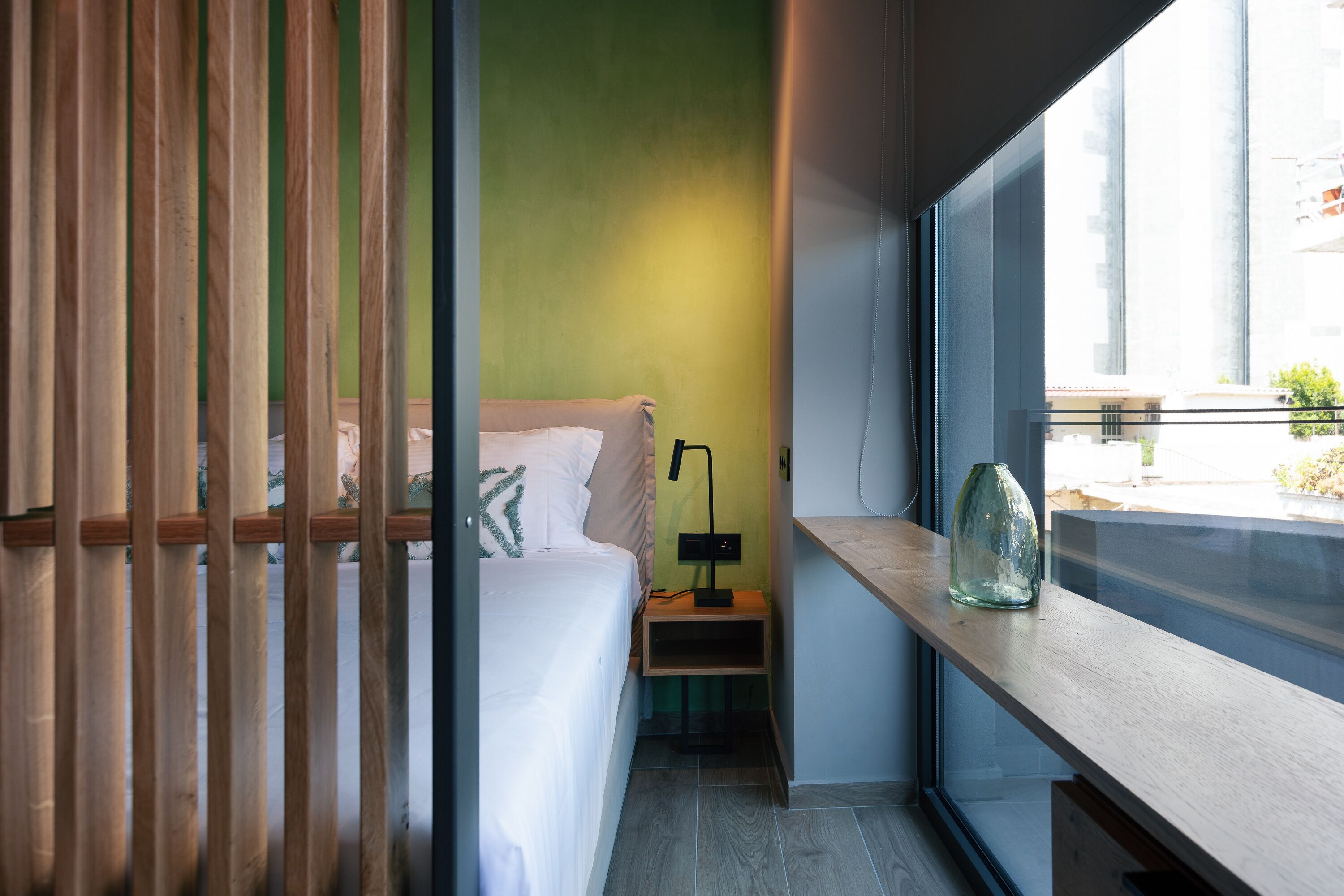 A modern bedroom with a bed, nightstand, and a window with a view of buildings.