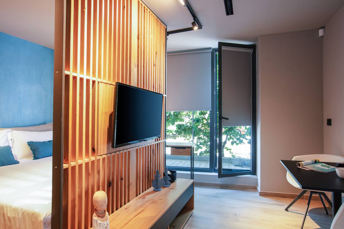 Un dormitorio moderno con cama, un separador de madera, televisor, escritorio y vistas al exterior.