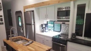 Une cuisine de taille réduite, dotée d’un plan de travail en bois, d’appareils électroménagers en acier inoxydable et de meubles de rangement blancs.