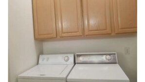 A laundry area with two white washing machines and wooden cabinets above. - Modern 2 bedroom. Minutes airport & ferry (Juneau)
