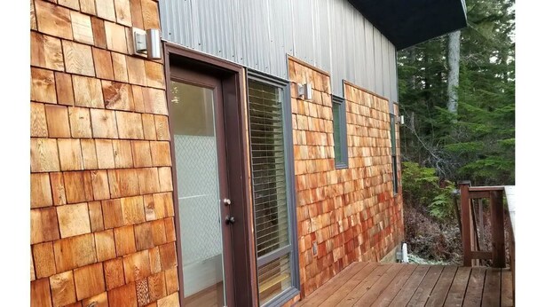 A wooden deck with a door and windows, surrounded by a forest. - Modern 2 bedroom. Minutes airport & ferry (Juneau)
