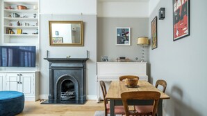 A living room with a fireplace, a dining table, and a TV. - JOIVY Captivating 1-Bed Flat In Fulham (London)