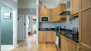 A modern kitchen with wooden cabinets, a microwave, and a stove. - JOIVY Captivating 1-Bed Flat In Fulham (London)