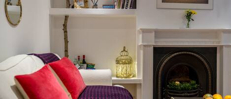 A living room with a white sofa, red and purple cushions, a fireplace, a bookshelf, and a TV on the wall.