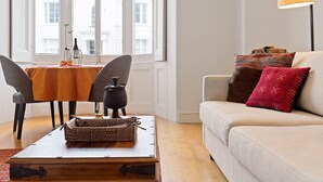 Ein Wohnzimmer mit einer Couch, einem Tisch mit Dekoration und einem Fenster mit Blick auf Gebäude.