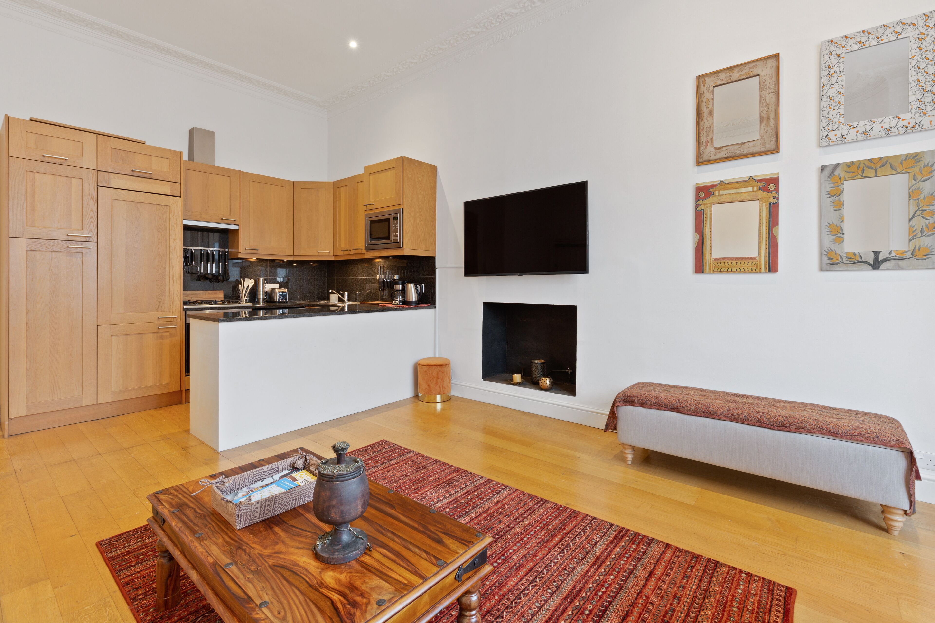 Una cocina moderna con armarios de madera, microondas integrado y una isla central. Hay un banco y una alfombra pequeña en la zona de estar.