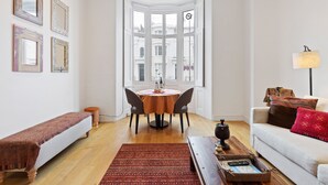 Ein Zimmer mit Erkerfenster, einem Esstisch mit Stühlen, einer Couch, einer Bank und einer Lampe.