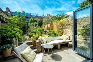 Eine Terrasse mit integriertem Sitzplatz, einem kleinen runden Tisch und Topfpflanzen.
