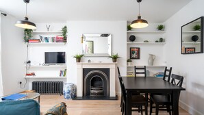 A modern living room with a fireplace, dining table, and seating area. - JOIVY Stylish 2-Bed Flat W/ Private Garden In Notting Hill, (London)
